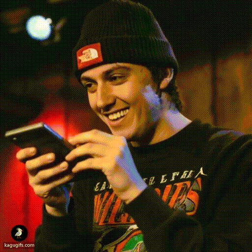 Young man in a navy beanie and graphic band tee holding a calculator, focused and calculating with an engaged expression.