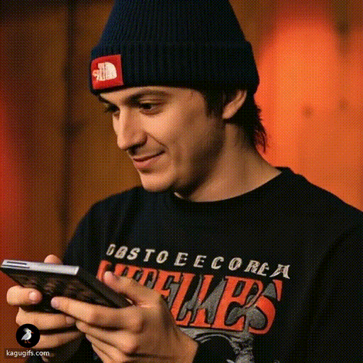 Young man in a navy beanie and graphic band tee holding a calculator, focused and calculating with an engaged expression.