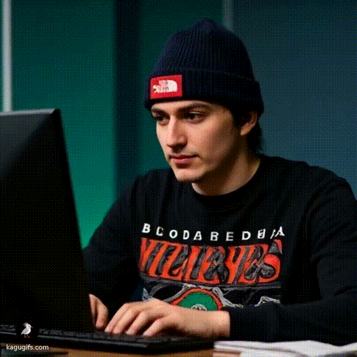 Young man in a navy beanie and graphic band tee typing intently at a Bloomberg terminal with fingers moving rapidly across the keyboard.