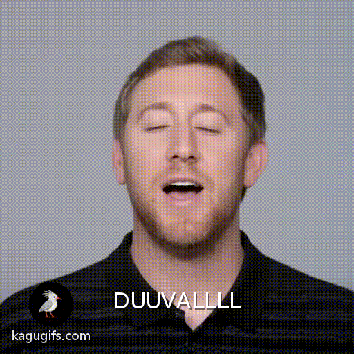 A man with light brown hair and stubble gently singing with a soft, warm expression, wearing a black striped polo shirt.