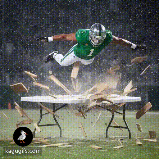 Muscular man in bright green football jersey with number 1, white pants with green stripes, black cleats, and chrome-visored helmet body diving from the sky through and slamming through a white plastic folding table, explosive impact with wooden debris flying, snow falling around the action.