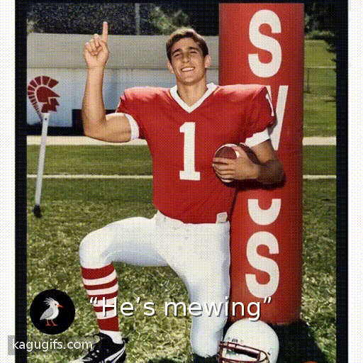 Athletic young man in red football jersey with white number 1 and white pants confidently raising his index finger upward in a number one gesture while holding a football, standing on a grass field with athletic energy and triumphant posture.