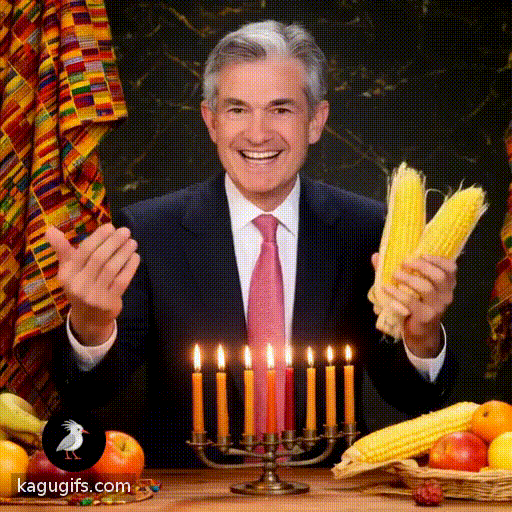 Jerome Powell, distinguished man with silver-gray hair, wearing a dark navy suit, white dress shirt, and red patterned tie, joyfully celebrating Kwanza with animated gestures, lighting the kinara candles, smiling warmly while holding traditional corn and fruit, moving rhythmically in festive celebration with colorful kente cloth draped nearby.