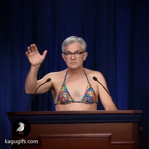 Jerome Powell, gray-haired man with glasses and serious expression, wearing a colorful bikini, gesturing confidently while speaking at a wooden podium with microphones.